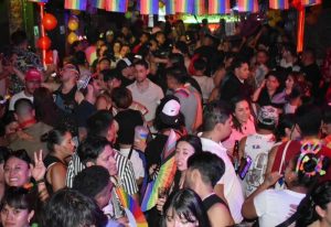El Pecado Gay Bar in Mexico: A crowded scene with many people, rainbow flags, and balloons. Nightlife for gay men's travel advice.
