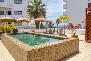 Rooftop pool at Amapas Apartments, a gay-friendly hotel in Puerto Vallarta. Lounge chairs, umbrellas, and palm trees offer a relaxing vacation vibe.