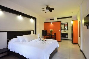Beach Energy Hotel by BFH: Gay-friendly hotel room interior. Bed with swan towels, orange accent wall, and open bathroom. Modern design.