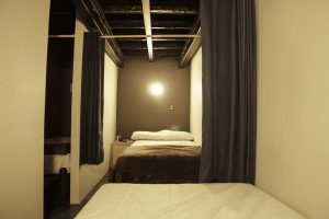 Interior of a gay-friendly capsule hostel. Sleeping pod with bed, curtain, and bedside table. Budget-friendly travel accommodation.