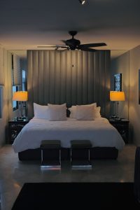 Casa Mannach's gay-friendly hotel room: King bed with padded headboard, ceiling fan, bedside tables with lamps, and two stools at the bed's foot.
