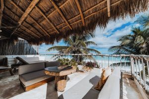 Dune Boutique Hotel's gay-friendly party zone: terrace view. Thatched roof, ocean vista, stylish outdoor furniture. Tropical paradise vibes.