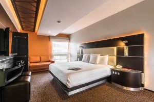 Exe Cities Reforma gay-friendly hotel room. Modern design, king bed, orange accent wall, and sofa. Ideal for gay travelers in Mexico City.