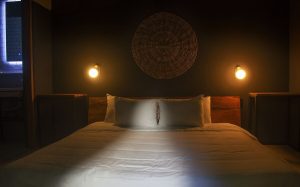 Loba Tulum Male Only gay-friendly hotel room. Bed with white sheets, two pillows, woven wall decor, and warm lighting. Gay travel lodging.