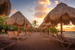 Beach at Platinum Yucatan Princess All Inclusive Suites Resort Adults Only. Thatched umbrellas and lounge chairs on the sand at sunset. Gay-friendly.