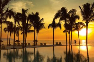 Secrets Vallarta Bay Resort all-inclusive adults-only gay-friendly hotel at sunset. Palm trees, pool, ocean view. Romantic travel.