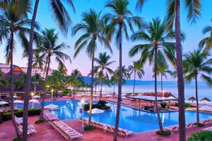 Sheraton Buganvilias Resort pool at dusk. Gay-friendly hotel with palm trees, lounge chairs, and ocean view. Perfect for gay travel.
