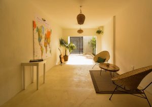 Stay Tropical gay-friendly hotel lobby. World map, guitar, and wicker chairs create a relaxed vibe. Perfect for gay men's travel adventures.