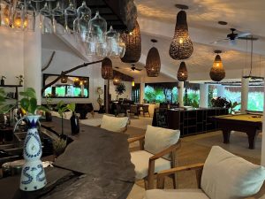 Interior of The Beach Tulum Hotel, a gay-friendly hotel. Bar, pool table, and dining area with woven light fixtures. Tropical, relaxed vibe.
