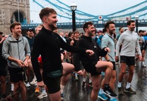 Gayns Free Saturday Queer Social Run Club: Group of gay men warming up before a run near Tower Bridge in London. Community and travel.