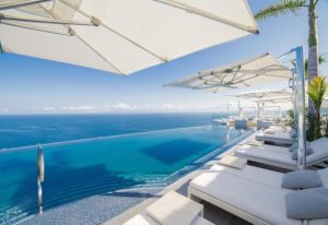 Hotel Mousai Adults-Only, a gay-friendly luxury hotel in Punta Mita. Infinity pool overlooking the ocean with lounge chairs and umbrellas.