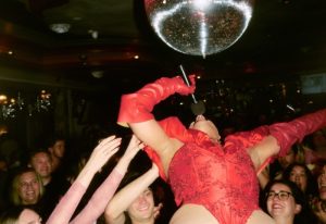 Imperial Erskineville Sydney: Drag queen in red performs under a disco ball, cheered on by a crowd. Gay travel nightlife scene.
