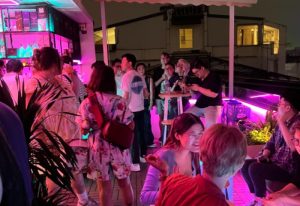Rooftop bar in Hanoi, Vietnam, with a diverse crowd of people enjoying drinks and socializing under colorful neon lights. Gay travel nightlife.