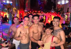 Space Hair Salon and Bar: Shirtless men pose at a gay bar. Festive atmosphere, possibly in Southeast Asia. Gay travel advice.