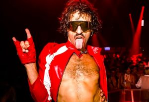 Studland Soho: Man at London's queer rave party. Red jacket, sunglasses, tongue out, rock on hand gesture. Best gay event.