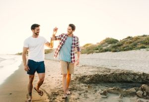 Two friends walking beach in Tulum, Mexico. Gay travel guide shows two men enjoying beers on the beach. Gay Tulum travel.