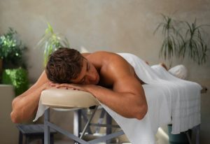 Beijing male massage: Man relaxing at spa. Side view of a man lying on a massage table covered with a white towel, eyes closed, relaxing.