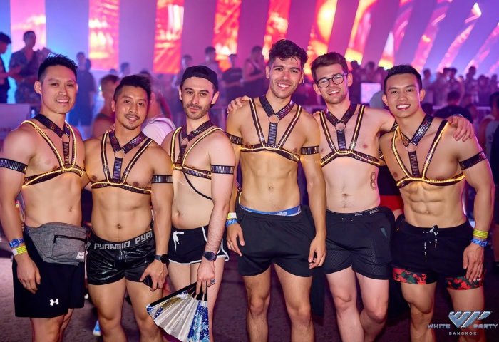 Gay men at White Party Bangkok. Six shirtless men pose in harnesses and shorts at the gay travel event. Nightlife and travel for gay men.