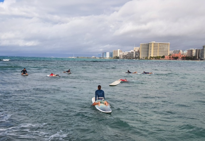 Honolulu surfing lesson in Waikiki. Surfers in the ocean with the Honolulu skyline in the background. Fabulous experience for gay men travelers.