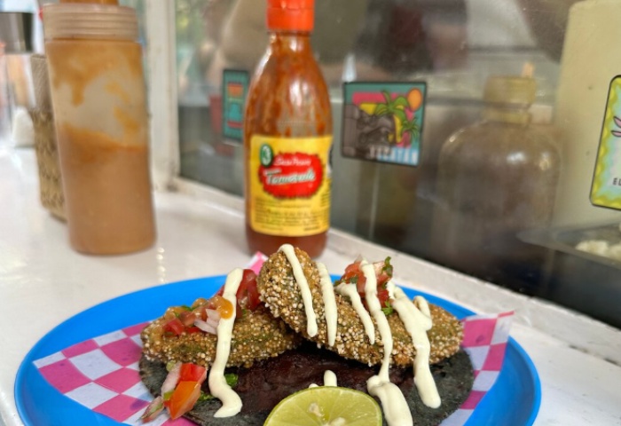 Mexico City LGBT-friendly veggie street eats: A blue corn tortilla taco with fried avocado, salsa, crema, and lime. Hot sauces in the background.