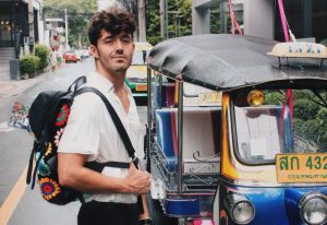 Gay traveler, Benjamin Thorpe, in Bangkok, Thailand. Holiday Inn Express Bangkok Sathorn in background. Tuk-tuk taxi and backpack.