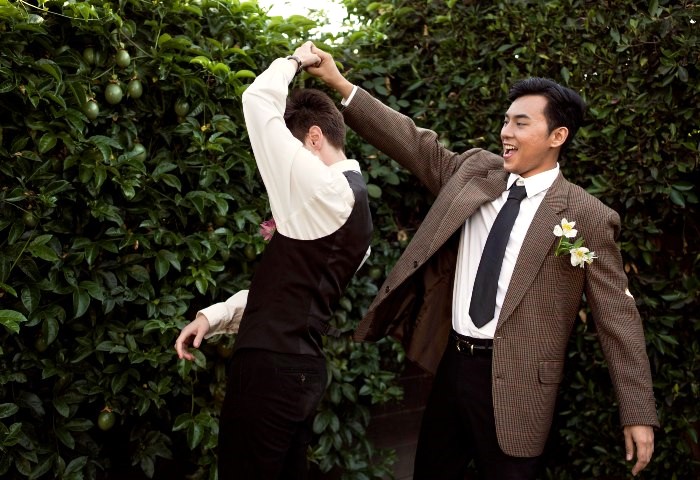 Cute gay couple dancing at their Bangkok wedding. Two grooms celebrate love, happiness, and commitment. Medium shot.