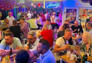 Gay bar scene at 3 Monkeys in Torremolinos. Crowded outdoor seating area with men enjoying drinks. Popular gay nightlife destination.