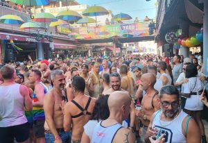 Crowd at Bar Junior, a gay bar in Gran Canaria. Rainbow umbrellas decorate the street. Gay travel destination.