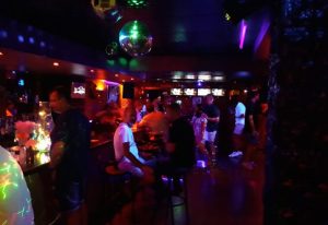 Benidorm gay party at Mercury Bar. People drinking, disco balls, and colorful lights create a vibrant atmosphere. Nightlife scene.