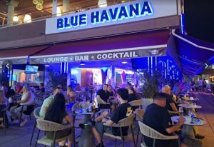 Blue Havana gay bar in Gran Canaria. Lounge bar with cocktails. People sit at tables outside. Nightlife scene. Gay travel.