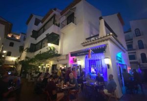 Boomerang Gay Bar in Torremolinos. Outdoor seating area at night. Rainbow flag visible. Gay travel advice. Gay bar nightlife.