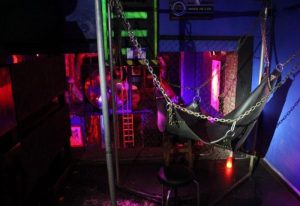 Inside Open Mind Gay Cruise Club in Barcelona, a dark room with a leather sling hanging from chains, lit with red and purple lights.
