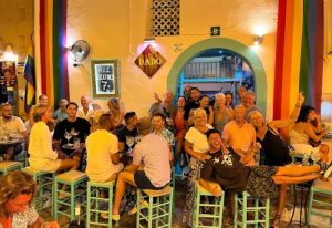Dado Bar, gay bar in Ibiza. People enjoying drinks, rainbow flag, and vibrant nightlife. Gay travel destination.