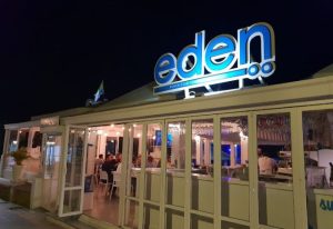 Exterior of Eden Nightclub, a gay beach club in Torremolinos, Spain. Lit up at night with a rainbow flag on the roof. Outdoor dining.