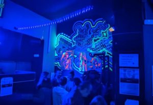 Interior of GRIS Gay Bar in Madrid, Spain. People gather under neon art and blue lights, enjoying the atmosphere of a popular gay nightlife spot.