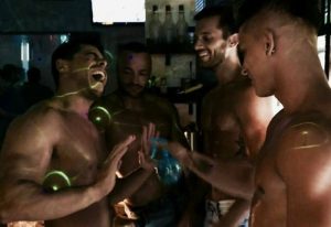 Gay nightlife in Madrid: Shirtless men laugh at La Kama Cafe, a popular gay bar. Gay travel advice for a fun night out in Spain.