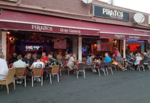 Pirates Bar Gran Canaria, a popular gay bar in Gran Canaria, Spain. Men sit at tables outside under a red awning, enjoying drinks.