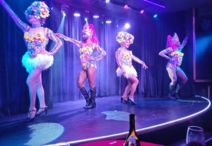Queenz Cabaret show at a gay bar in Sitges. Four drag queens on stage in colorful costumes with flower headpieces, performing for the audience.