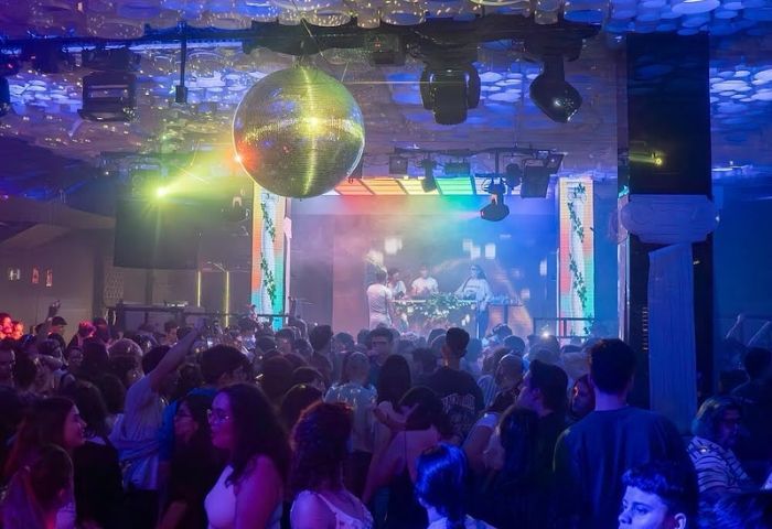 Safari Disco Club, Barcelona. Gay club scene with a crowd dancing under a disco ball. DJs performing on stage, colorful lighting.
