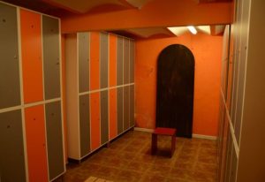 Locker room at Sauna Lavapies, a gay sauna in Madrid. Orange walls, lockers with orange and gray doors, and a dark arched doorway.