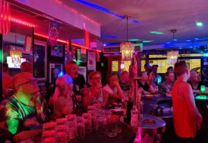 Inside Sensations gay bar in Benidorm, Spain. People at the bar, glasses, bottles, colorful lights. Gay travel destination, nightlife.
