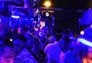 Crowded Sixta Bar, a gay bar in Madrid. Blue lighting illuminates diverse men in a lively nightlife scene. Gay travel advice.