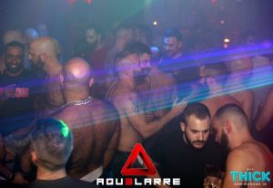 Crowd at THICK Gay Bar in Madrid. Shirtless men, beards, and tattoos visible. Nightlife scene, LGBTQ+ travel, gay bar, Madrid nightlife.
