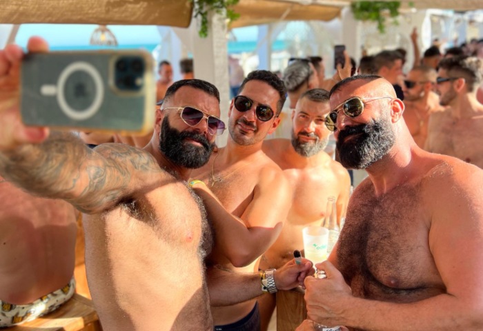 Gay men taking a selfie at a Torremolinos gay bar. Group of shirtless men enjoying a sunny day at a beach party. Image.jpg.