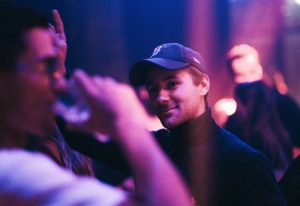 Man in baseball cap at Ibiza gay bar. Nightlife scene with purple and blue lighting. Gay travel advice, Peter Bucks.