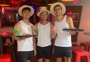 Three men with hats in a Sitges gay bar. Waiters serving food. Gay travel in Sitges, Spain. rsw_1160h_1263.jpg. Gay bars in Sitges.
