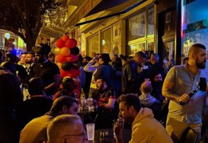 Gay bar TR3S in Lisbon, Portugal. Outdoor patio area filled with gay men drinking and socializing at night. Balloons decorate the entrance.