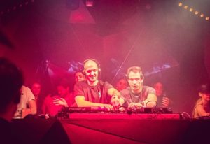 D9-Dark-Nine Budapest: Two DJs performing at a gay club in Budapest, bathed in red light, creating an energetic atmosphere. Gay travel advice.