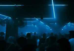 Dirty Cash gay bar in Budapest. Crowd of people under blue neon lights. Gay travel advice for nightlife in Hungary's capital.
