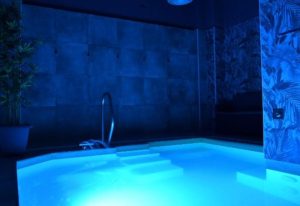 Fenix Sauna Milano: Blue-lit jacuzzi, steps, and handrail. Gay sauna travel advice. Relaxing spa experience.